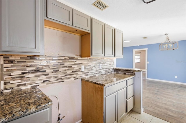 kitchen featuring decorative light fixtures, light tile patterned floors, backsplash, dark stone counters, and gray cabinets