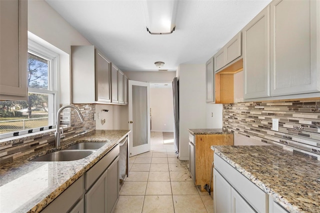 kitchen featuring light stone countertops, dishwasher, light tile patterned floors, decorative backsplash, and sink