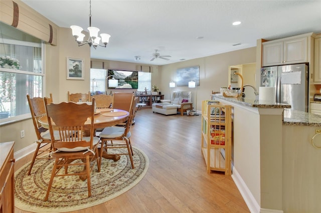 dining room with sink, ceiling fan with notable chandelier, and light wood-type flooring