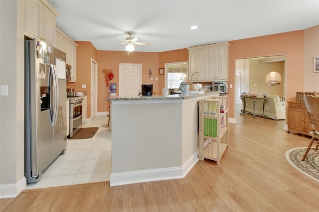 kitchen with light stone countertops, appliances with stainless steel finishes, ceiling fan, cream cabinets, and light hardwood / wood-style flooring