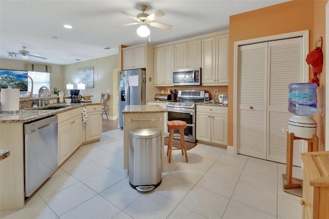 kitchen with light stone countertops, appliances with stainless steel finishes, sink, cream cabinetry, and a center island