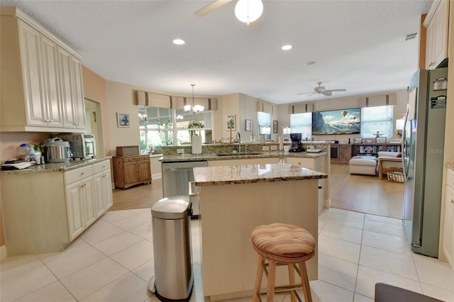 kitchen with kitchen peninsula, stainless steel appliances, pendant lighting, light tile patterned floors, and cream cabinets