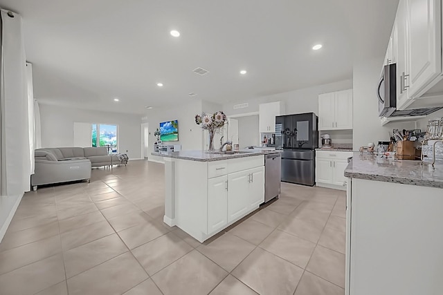 kitchen featuring a kitchen island with sink, white cabinets, light tile patterned floors, light stone countertops, and stainless steel appliances