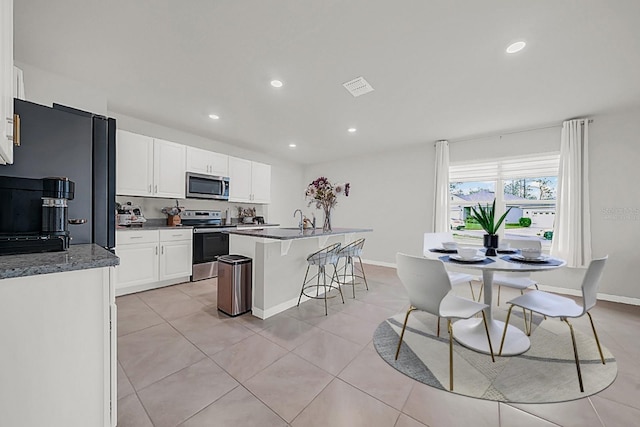 kitchen featuring appliances with stainless steel finishes, sink, light tile patterned floors, white cabinets, and an island with sink