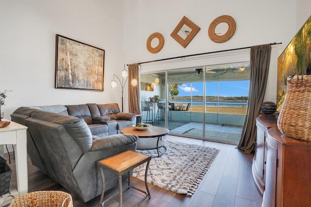 living room with ceiling fan, a water view, wood-type flooring, and a high ceiling