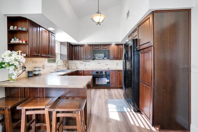 kitchen featuring a kitchen breakfast bar, light hardwood / wood-style flooring, kitchen peninsula, decorative light fixtures, and black appliances