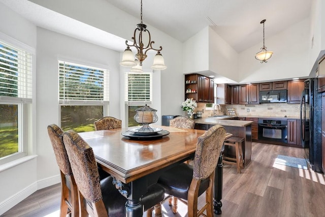 dining area featuring sink, a chandelier, vaulted ceiling, and light wood-type flooring