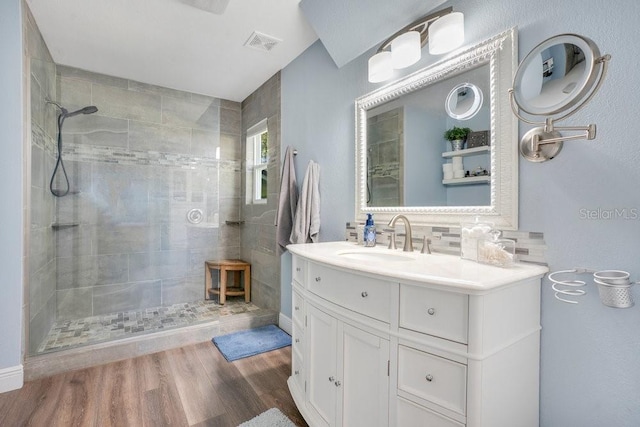 bathroom with vanity, a tile shower, wood-type flooring, and tasteful backsplash