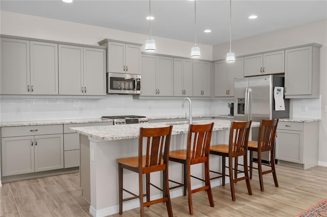 kitchen with decorative light fixtures, stainless steel appliances, gray cabinets, and an island with sink