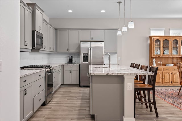 kitchen featuring light stone countertops, gray cabinetry, a breakfast bar, stainless steel appliances, and a center island with sink