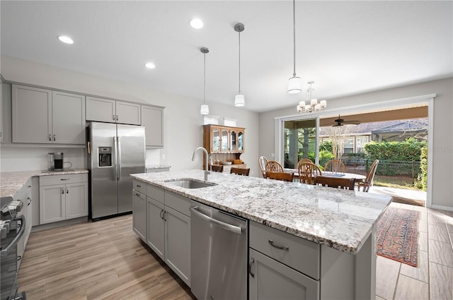 kitchen with ceiling fan with notable chandelier, hanging light fixtures, gray cabinets, an island with sink, and stainless steel appliances