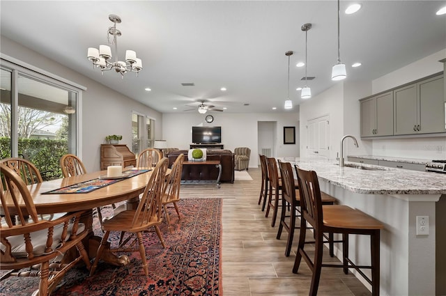 dining room featuring ceiling fan with notable chandelier, sink, and light hardwood / wood-style flooring