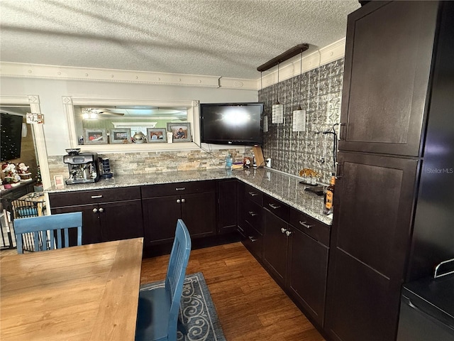 kitchen featuring dark wood-type flooring, decorative backsplash, a textured ceiling, light stone counters, and dark brown cabinetry