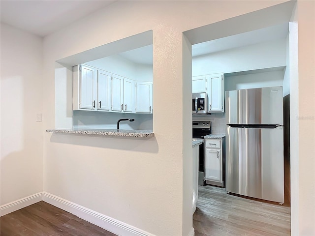 kitchen featuring decorative backsplash, appliances with stainless steel finishes, light stone countertops, light hardwood / wood-style flooring, and white cabinetry