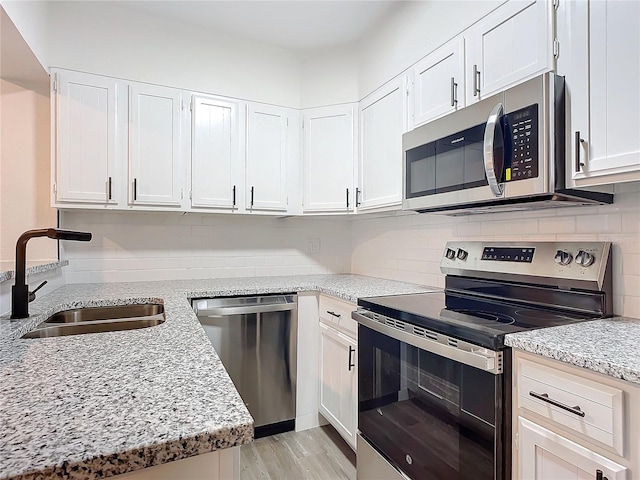 kitchen with light stone counters, stainless steel appliances, sink, light hardwood / wood-style floors, and white cabinetry