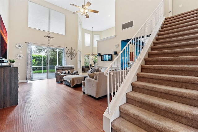 living room with ceiling fan with notable chandelier, wood-type flooring, and a high ceiling