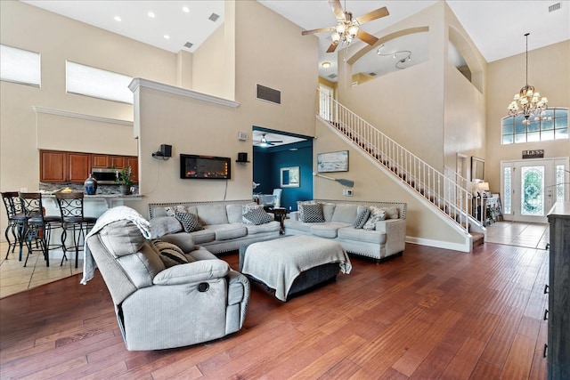 living room with a towering ceiling, ceiling fan with notable chandelier, and hardwood / wood-style flooring