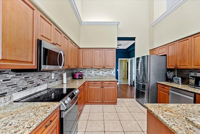 kitchen with decorative backsplash, appliances with stainless steel finishes, light stone countertops, a high ceiling, and light tile patterned flooring