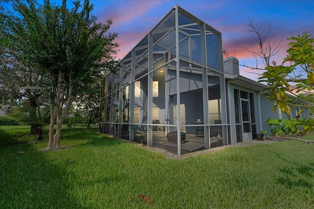 back house at dusk featuring a lanai, a yard, and a patio