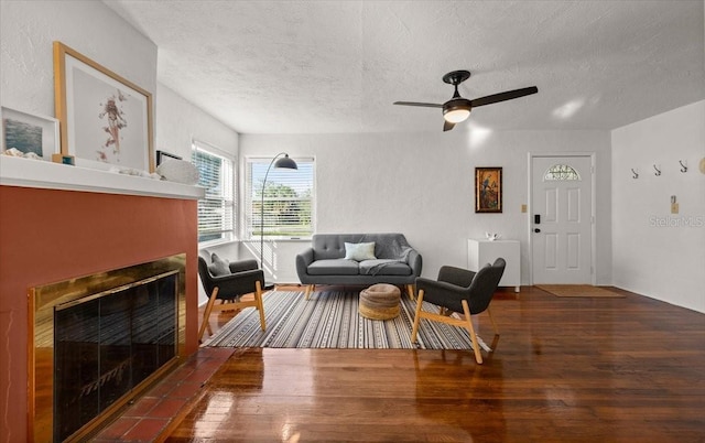 living room featuring ceiling fan, dark hardwood / wood-style flooring, a textured ceiling, and a tile fireplace