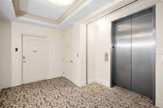 entrance foyer featuring elevator, a tray ceiling, and light colored carpet