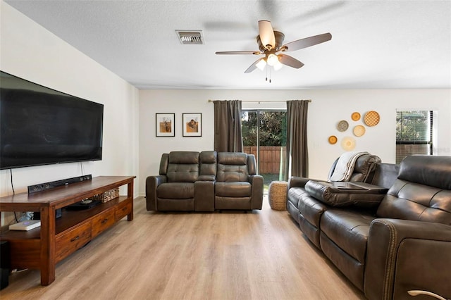 living room featuring ceiling fan, light hardwood / wood-style flooring, a healthy amount of sunlight, and a textured ceiling