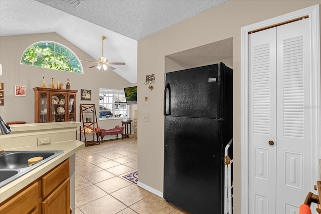 kitchen featuring ceiling fan, sink, black fridge, vaulted ceiling, and light tile patterned flooring