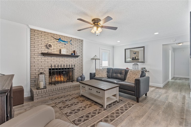 living room with a textured ceiling, ornamental molding, light wood-type flooring, a fireplace, and ceiling fan