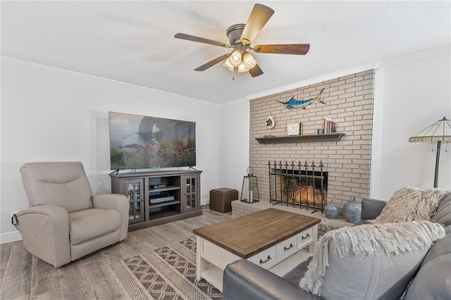 living room with a textured ceiling, a fireplace, ceiling fan, light hardwood / wood-style flooring, and crown molding