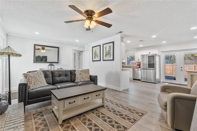 living room with a textured ceiling, light hardwood / wood-style flooring, french doors, and ornamental molding