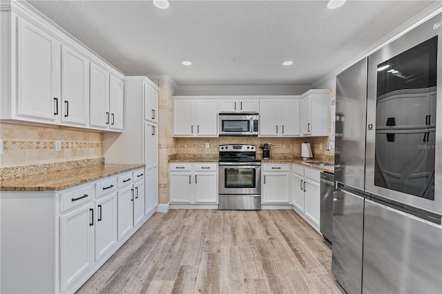 kitchen with light stone countertops, stainless steel appliances, crown molding, white cabinetry, and sink