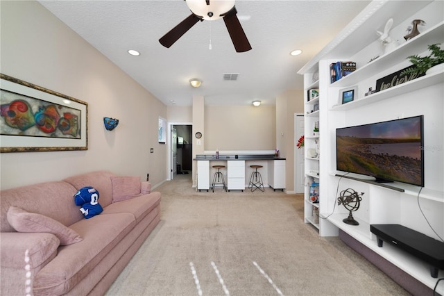 living room with light carpet, ceiling fan, and a textured ceiling