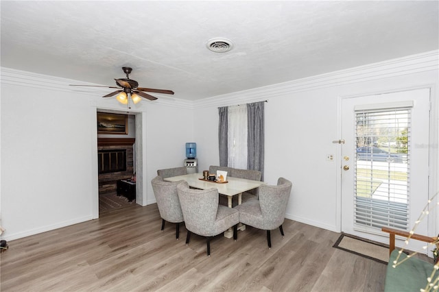 dining room featuring ceiling fan, ornamental molding, wood-type flooring, and a brick fireplace