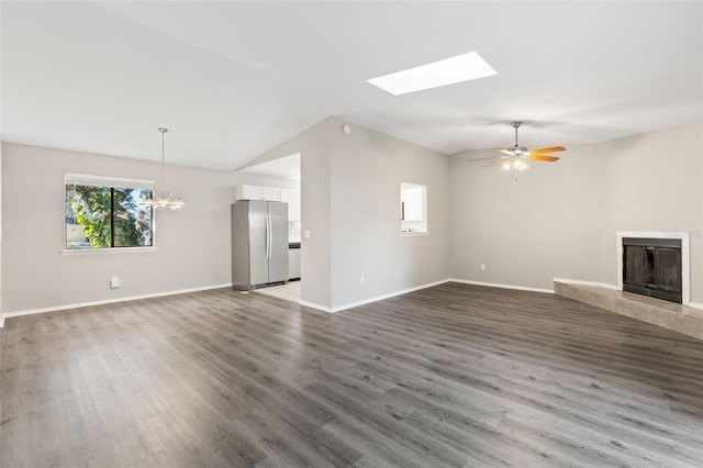 unfurnished living room with vaulted ceiling, ceiling fan with notable chandelier, a tile fireplace, and hardwood / wood-style flooring