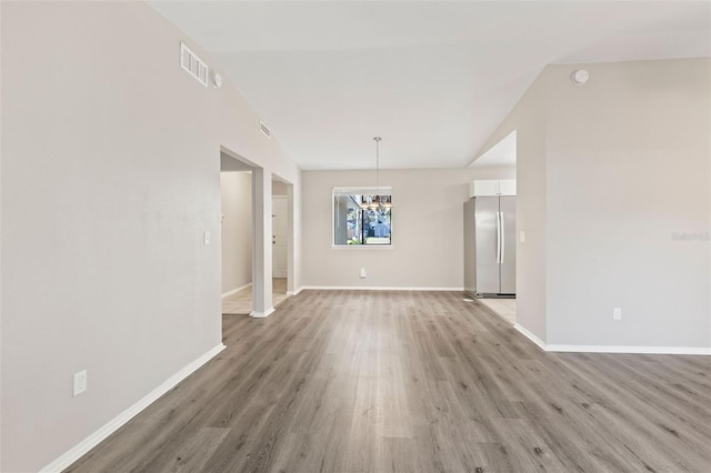 unfurnished living room with hardwood / wood-style flooring, a chandelier, and lofted ceiling