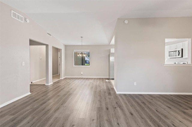 spare room with dark wood-type flooring, lofted ceiling, and a notable chandelier