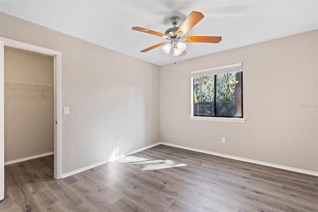 unfurnished bedroom with a closet, ceiling fan, a spacious closet, and wood-type flooring