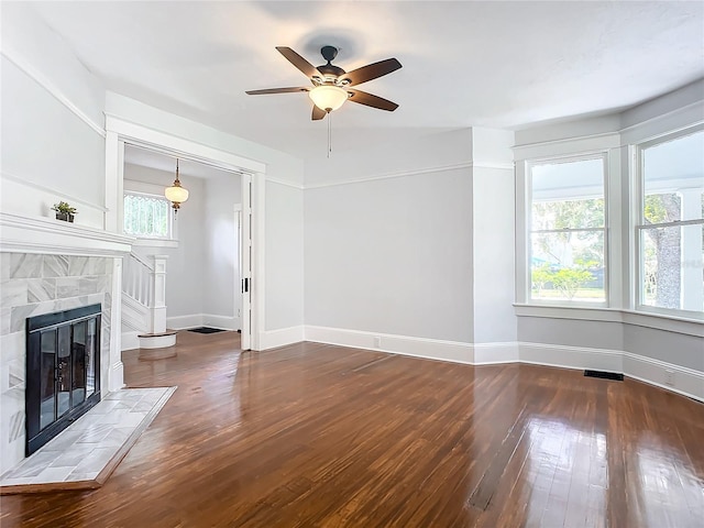 unfurnished living room featuring a wealth of natural light, ceiling fan, dark wood-type flooring, and a tile fireplace