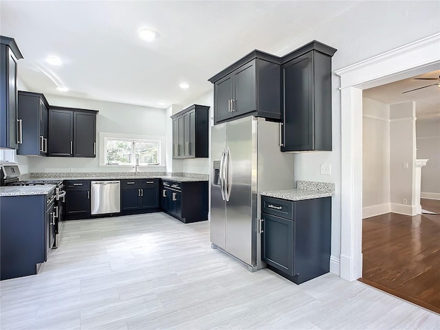 kitchen with ceiling fan, light stone counters, light wood-type flooring, and appliances with stainless steel finishes