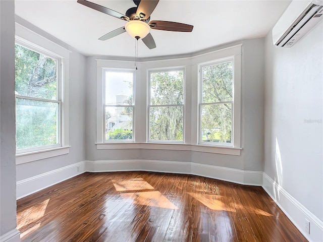 empty room with dark hardwood / wood-style flooring, a wall unit AC, plenty of natural light, and ceiling fan