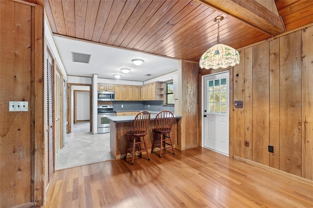 kitchen with a breakfast bar, light brown cabinets, appliances with stainless steel finishes, decorative light fixtures, and kitchen peninsula