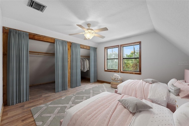 bedroom featuring hardwood / wood-style floors, two closets, vaulted ceiling, ceiling fan, and a textured ceiling