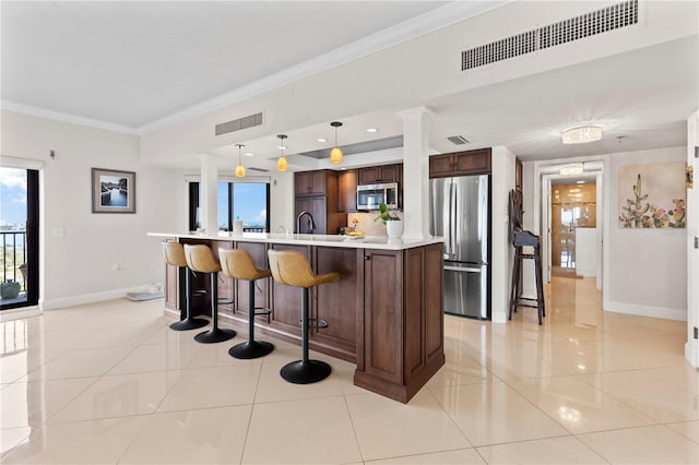 kitchen featuring appliances with stainless steel finishes, decorative light fixtures, light tile patterned floors, and a kitchen island with sink