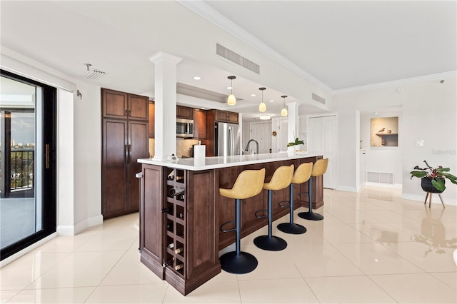 kitchen with appliances with stainless steel finishes, ornamental molding, pendant lighting, light tile patterned floors, and a kitchen island