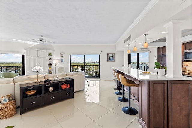 kitchen with decorative columns, crown molding, an island with sink, and decorative light fixtures