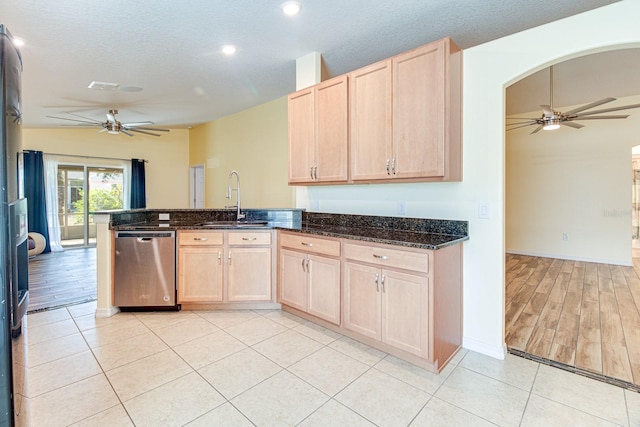 kitchen with dishwasher, light brown cabinets, dark stone counters, sink, and a textured ceiling