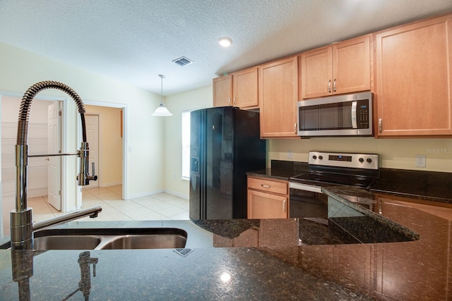 kitchen with appliances with stainless steel finishes, light brown cabinetry, a textured ceiling, light tile patterned floors, and hanging light fixtures