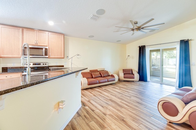 kitchen featuring light brown cabinets, stainless steel appliances, dark stone counters, and light hardwood / wood-style flooring