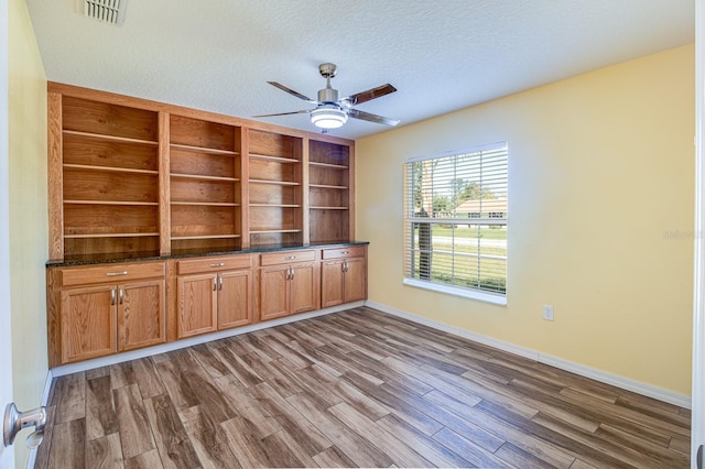 unfurnished living room featuring dark hardwood / wood-style floors, ceiling fan, built in features, and a textured ceiling