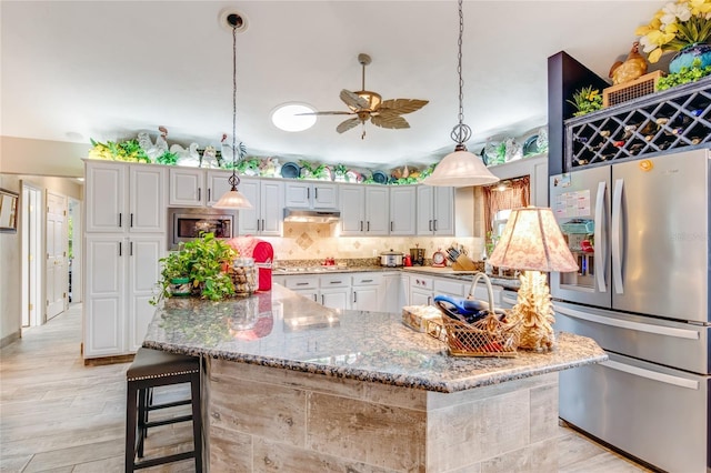 kitchen with backsplash, white cabinets, hanging light fixtures, a kitchen bar, and stainless steel appliances